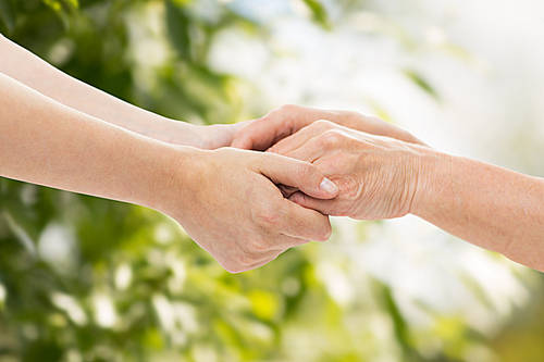 people, age, family, care and support concept-close up of senior woman and young woman holding hands over green natural background