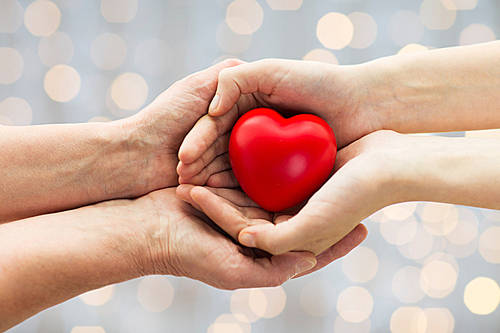 people, age, family, love and health care concept-close up of senior woman and young woman hands holding red heart over lights background