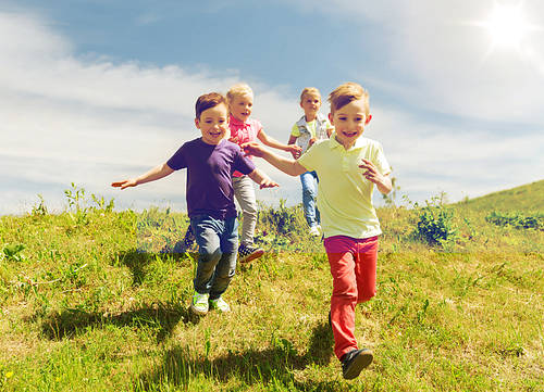 summer, childhood, leisure and people concept-group of happy kids playing tag game and running on green field outdoors