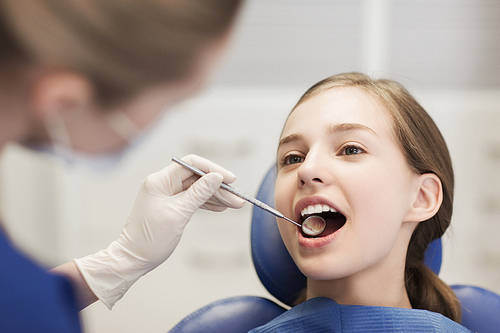 people, medicine, stomatology and health care concept-happy female dentist with mirror checking patient girl teeth up at dental clinic office