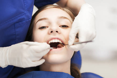 people, medicine, stomatology and health care concept-happy female dentist with mirror checking patient girl teeth up at dental clinic office