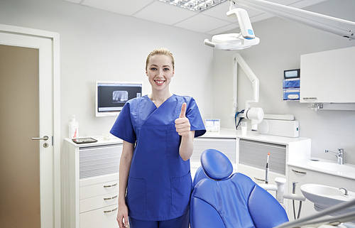 people, medicine, stomatology and healthcare concept - happy young female dentist showing thumbs up at dental clinic office