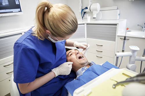 people, medicine, stomatology and health care concept - female dentist with dental mirror checking up male patient teeth at dental clinic office