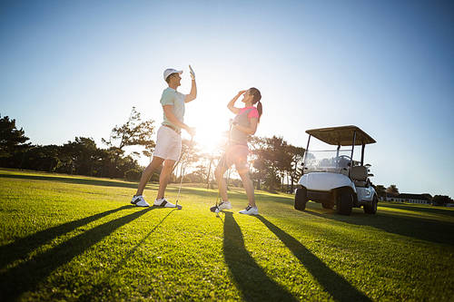 Full length of golf player couple giving high five while standing on field