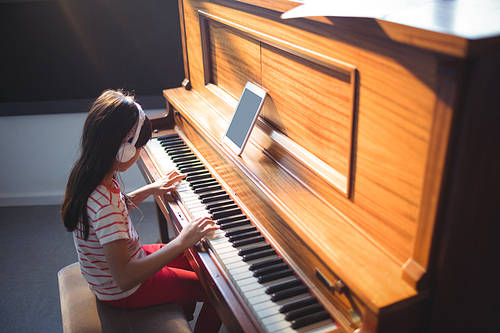 High angle view of concentrated girl wearing headphones while practicing piano in classroom at music school