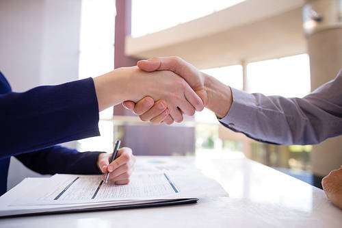 Close-up of businesswoman shaking hands with colleague at desk in conference center