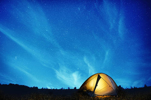 Illuminated yellow camping tent under stars at night