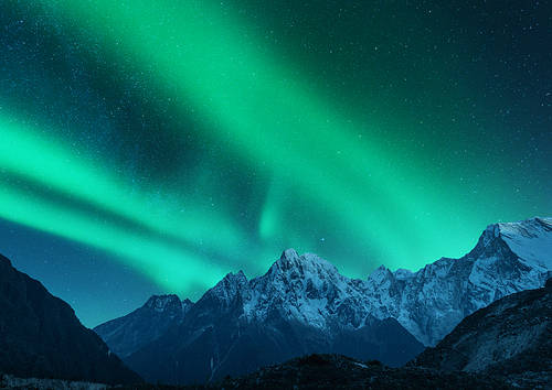 Aurora borealis above the snow covered mountain range in europe. Northern lights in winter. Night landscape with green polar lights and snowy mountains. Starry sky with aurora over the rocks. Space