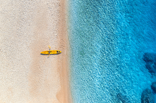 Aerial view of empty sandy beach with yellow canoe, sea coast with transparent blue water in sunny bright day in summer. Travel in Croatia. Top view of boats. Landscape with kayaks at sunset. Travel