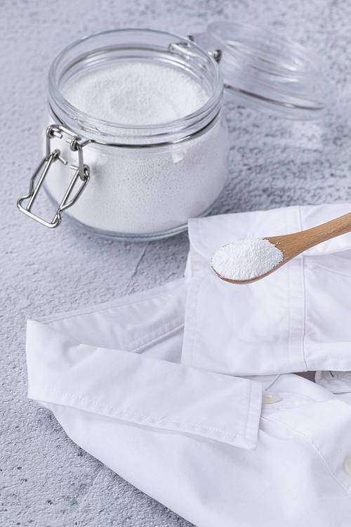 Zero waste - white shirt and glass bottle and wooden spoon with bicarbonate of soda, close-up