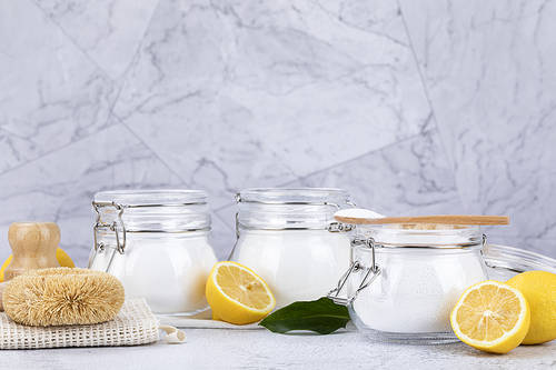 Zero Waste - Glass bottle and wooden spoon with bamboo cleaning brushes, lemon, natural loofahs and citric acid powder, baking soda and percarbonate powder on linen cloth