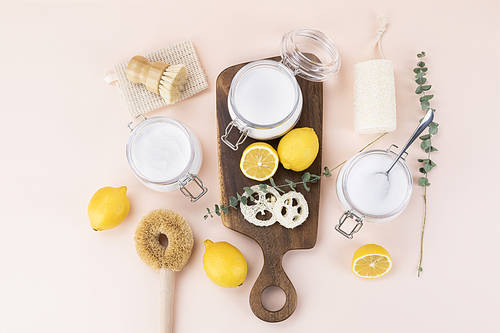 Zero Waste - Bamboo cleaning brushes, natural loofahs and lemon and glass jar with citric acid powder, baking soda and soda percarbonate powder on a wooden chopping board and top view of an iron and wooden spoon