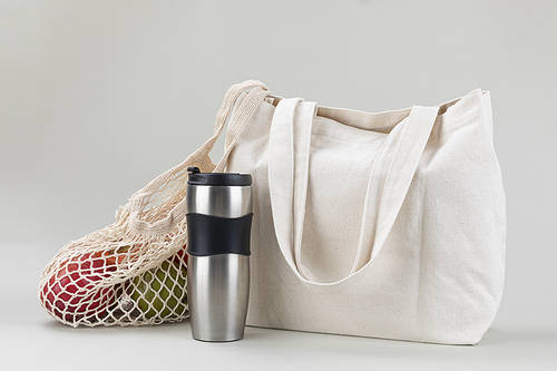 Zero waste - gray background, eco bag and net bag with fruits and tumbler