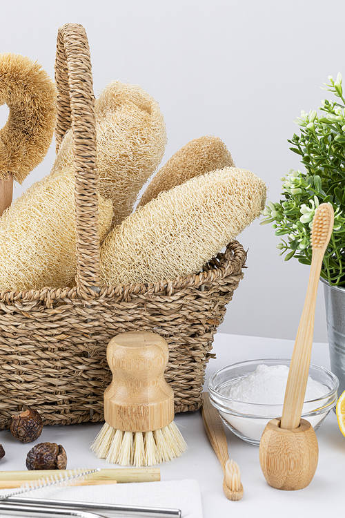 Zero Waste - Bamboo toothbrush and toothbrush holder placed in front of a basket with natural loofah and cleaning brush, close-up