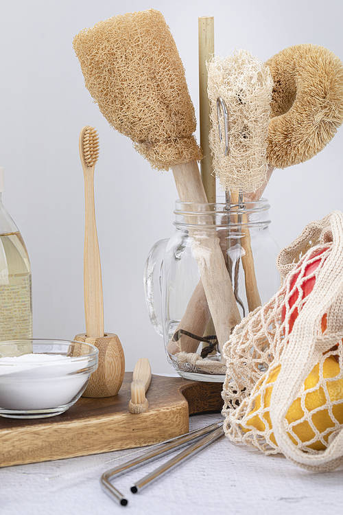 Zero waste-a glass bowl of baking soda on a wooden cutting board, bamboo toothbrush and toothbrush holder, net bag with fruit and stainless straws, close-up