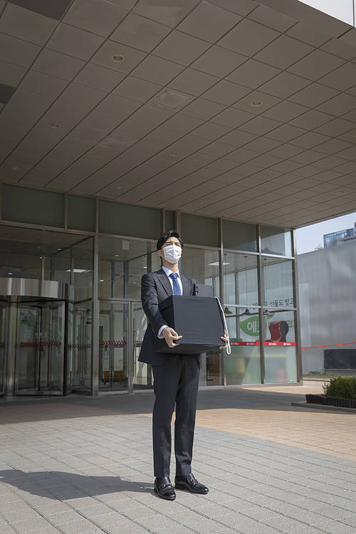 New Employees in the Corona Era-A young new employee wearing a mask looking away with luggage from the company