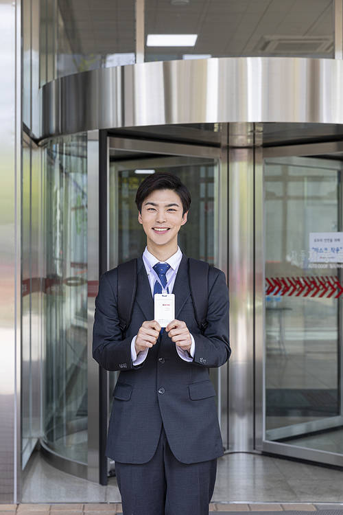 Young New Employee Day - Energetic young new employee holding employee ID in front of building