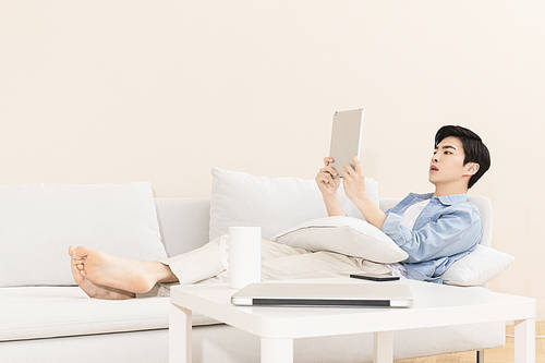 The wise life of a job seeker - a young man lying on the sofa and playing with a tablet pc