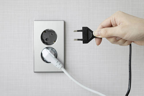 Energy Habits in Life - Plugged outlet and hand holding the outlet