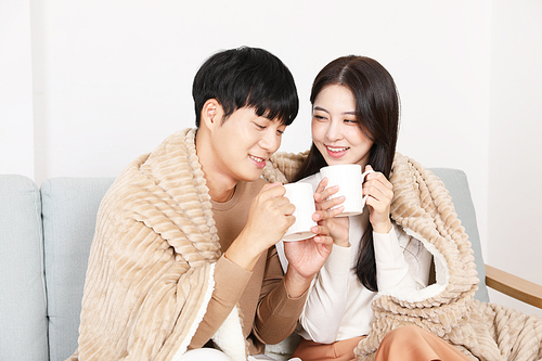 Lovers sitting on the sofa and drinking tea under a blanket