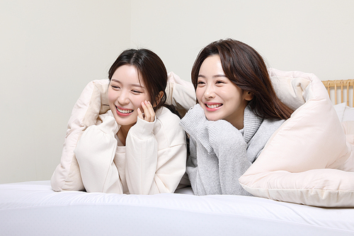 Winter indoor daily life_Photo of two women laughing while watching TV in bed