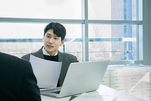 Two men _ A photo explaining while looking at a laptop and documents