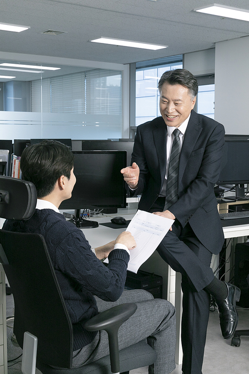 Two men_ sitting at a desk and talking about work