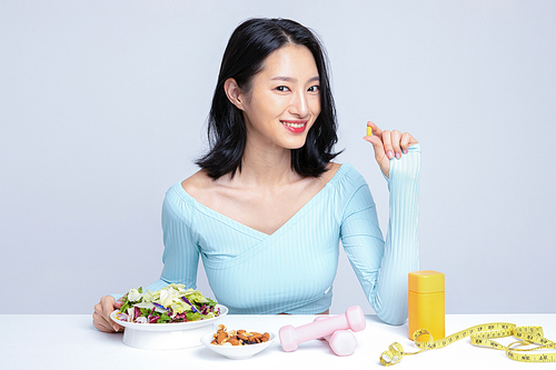 Healthy eating_Photo image of a woman holding a pill in front of diet and exercise equipment