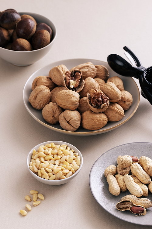 Chestnuts, walnuts, peanuts, and pine nuts are piled on each plate, and there is a nutcracker next to it.