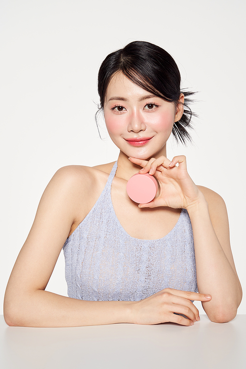 Asian woman smiling while holding a pink cushion compact