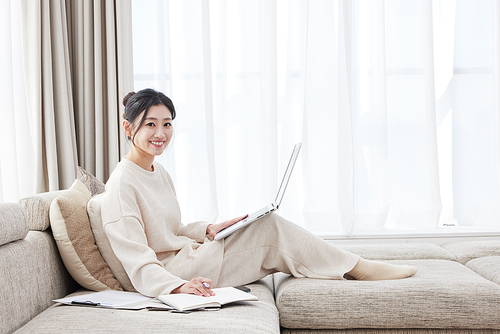 A woman smiling while leaning on a sofa with a laptop resting on her legs