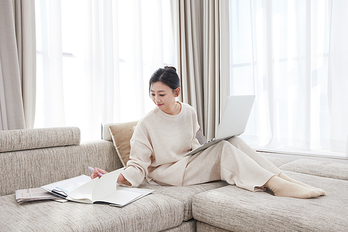 A woman leaning on a sofa and working while looking at a laptop and documents