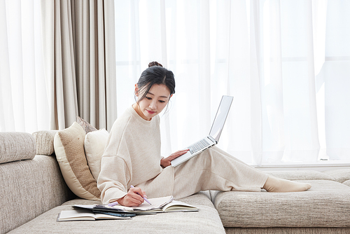 A woman leaning on a sofa, holding a pen and writing notes in a newspaper