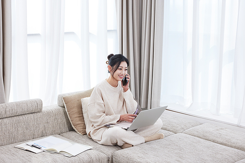 A woman sitting cross-legged on the sofa and working on her cell phone