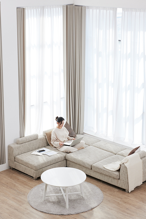 A woman sitting cross-legged on the sofa and working on a laptop