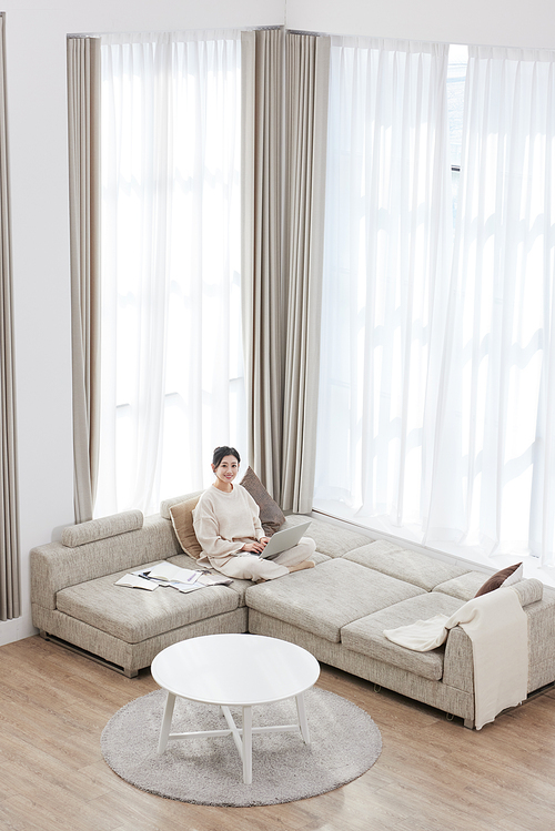 A woman sitting cross-legged on the sofa and using a laptop