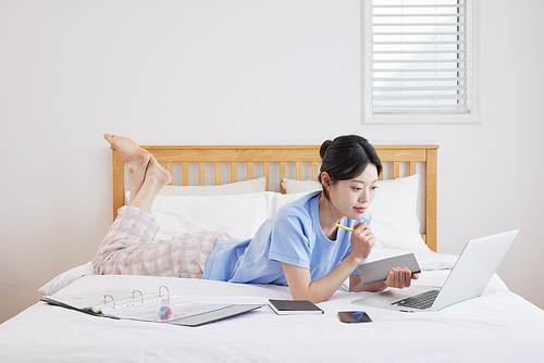 A woman lying face down on the bed and looking at a laptop