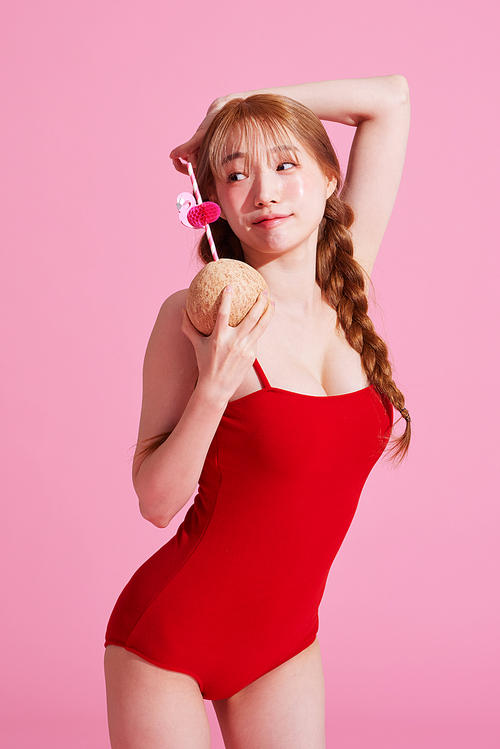 A Korean woman in her 20s wearing a monokini look and posing while holding a coconut drink.