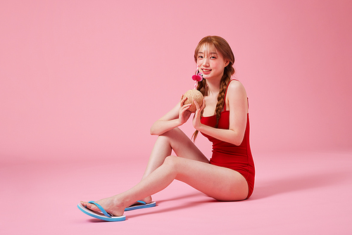 A Korean woman in her 20s wearing a monokini look sitting on the floor and holding a coconut drink
