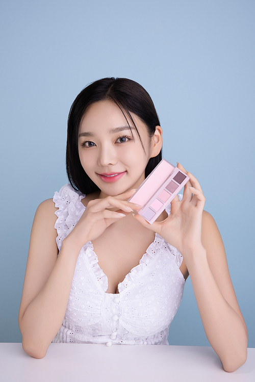 A woman in her 20s posing with a cool-toned color shadow palette.