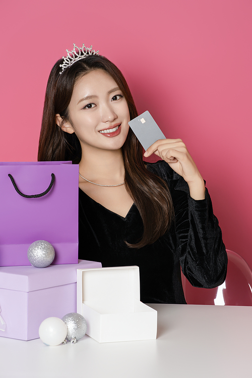 A woman in her 20s wearing a crown and posing in front of shopping bags and gift boxes