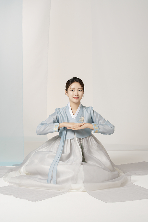 A beautiful woman wearing a luxurious and elegant hanbok sits and bows.