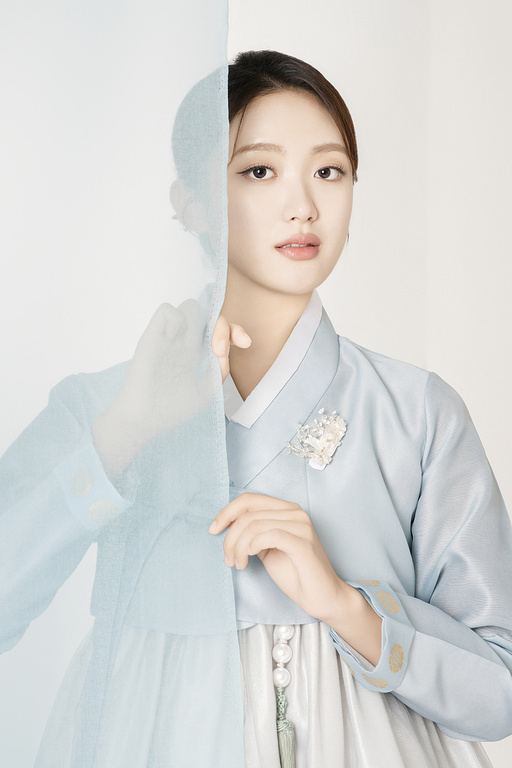 A beautiful woman wearing a luxurious and elegant Hanbok, standing behind a blue cloth