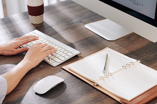 Hands of female entrepreneur sitting at office desk and working on computer