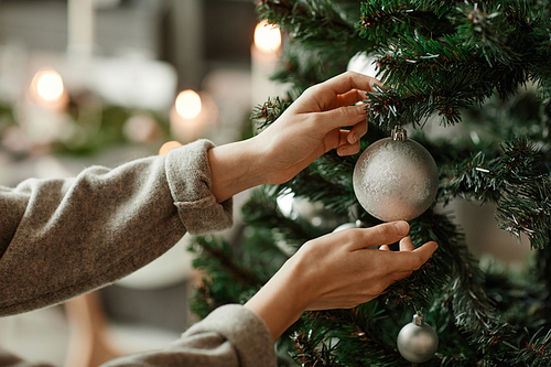 Side view close up of young woman decorating Christmas tree at home in elegant silver and gray tones, copy space