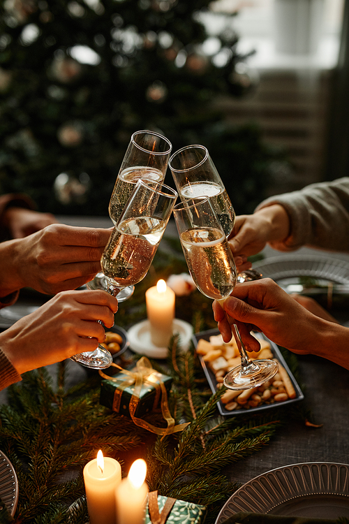 Vertical close up of four people enjoying Christmas dinner together and toasting with champagne glasses while sitting by elegant dining table with candles