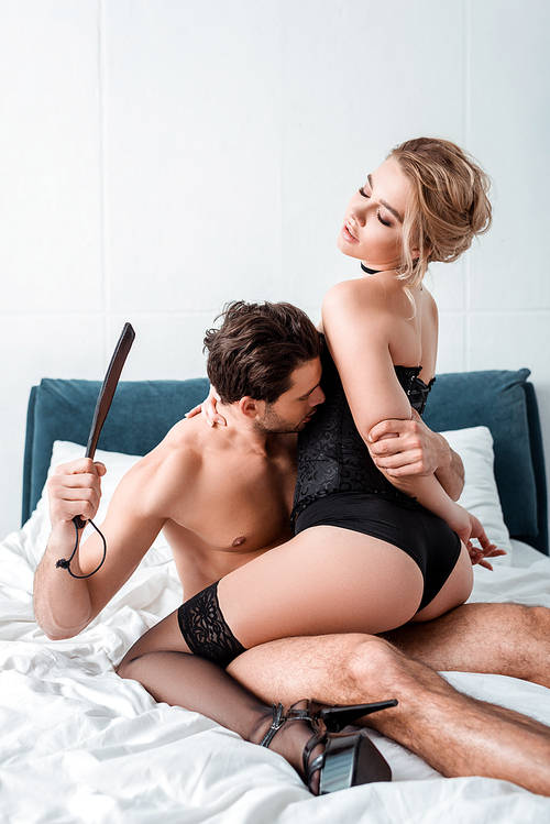 dominant man holding spanking paddle near submissive woman