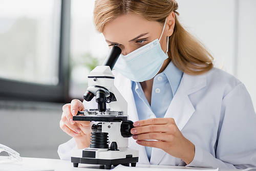 specialist in medical mask looking through microscope in laboratory