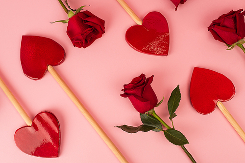 top view of heart-shaped lollipops near red roses on pink