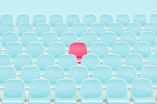 Singer red seat in the middle of light blue chair in stadium.